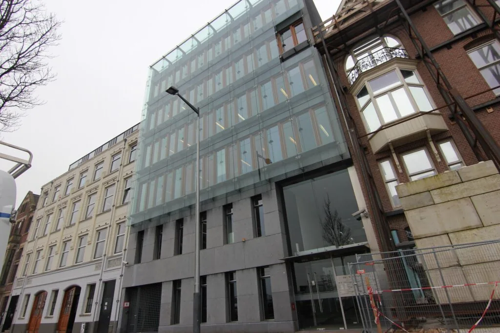 Modern kantoorgebouw met glazen gevel aan de De Ruijterkade in Amsterdam, omringd door oudere panden.